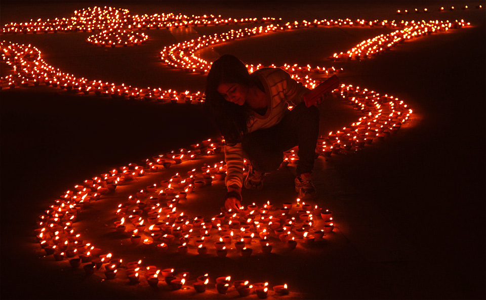 girl lights earthen lamps, india